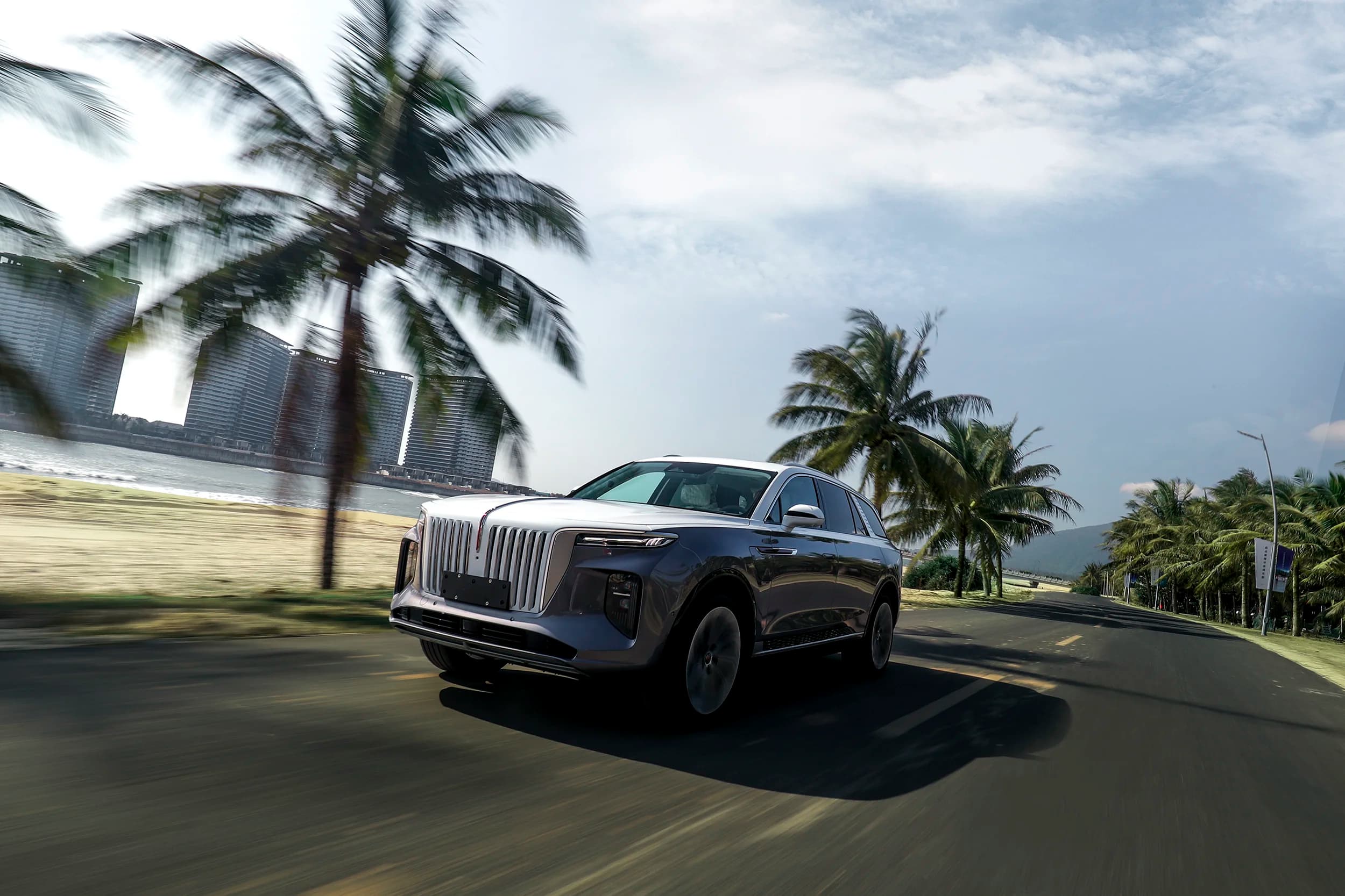 Silver Hongqi E-HS9 luxury SUV in motion on a palm-lined coastal road